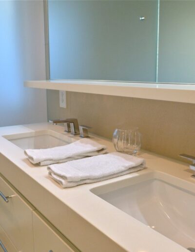 all white bathroom with dual vanity undermount sinks and frosted glass panel