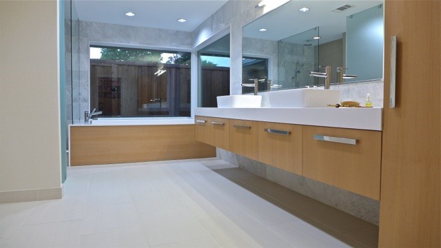 large bathroom with white countertops warm wood cabinetry, large windows, and large mirror