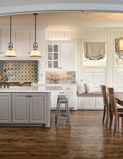 Large white kitchen with farmhouse feel, built-in seating, wood floors, black lights, and tile backsplashes