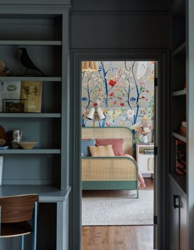 dark gray room looks into a bedroom with colorful bird painted walls