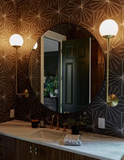 moody bathroom with geometric wallpaper, round vanity mirror, round glass wall sconces, and undermounted sink