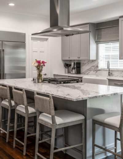 all white and light gray kitchen with contemporary island seating and large stove hood, stainless steel appliances, and white marble backsplash