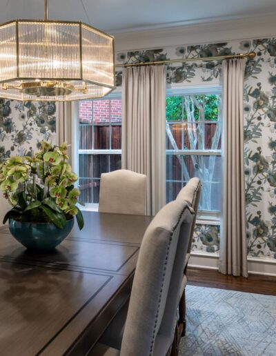 A dining room with floral wallpaper, wood floors, contemporary furnishings, and a gold modern chandelier