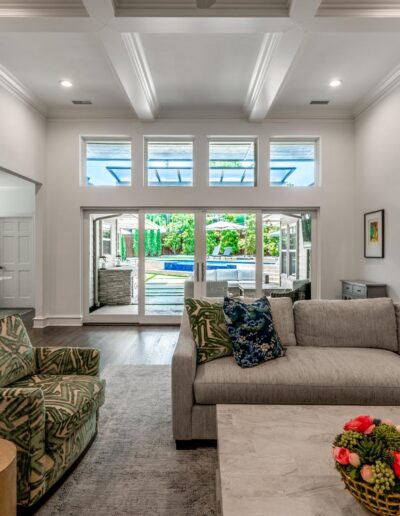 large white living room with high ribbed ceilings, arched doorways, and large windows looking out to the back deck