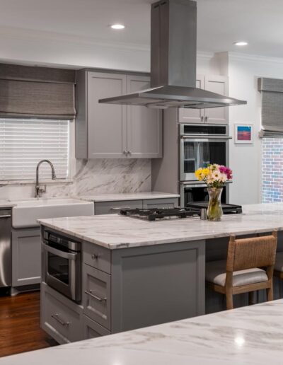 Large kitchen with white counters, gray shaker cabinets, an eat-in island, farmhouse sink, stainless steel appliances, and windows