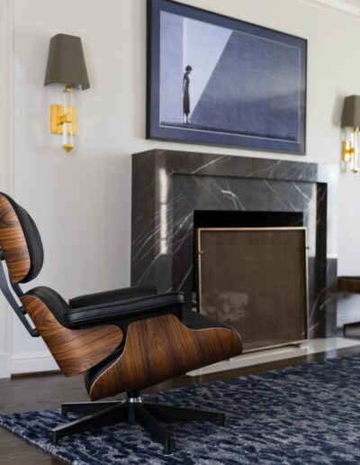 black marble fireplace in a white wall with an Eames style lounge chair and ottoman and wall sconces