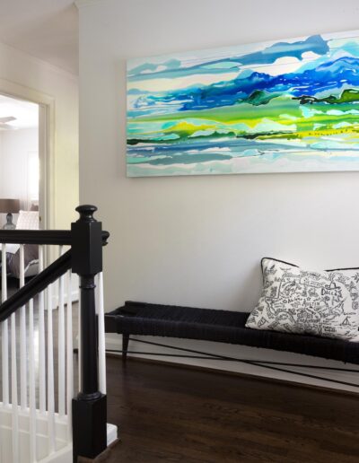 hall with painting and bench at top of white stairs with black handrail