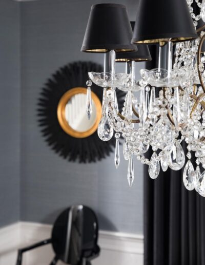 Crystal and gold chandelier with small black lampshades in a room with dark wall paper, curtains, and black furniture