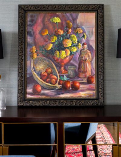 a framed still life painting and lamps sitting on a dark cabinet in front of a gray wall