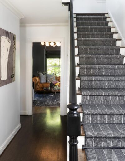 geometric painting across the hallway from a white stairway with wooden steps and a black handrail with a dark fabric runner