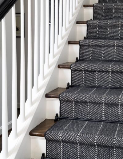 white stairway with wooden steps and a black handrail with a dark fabric runner