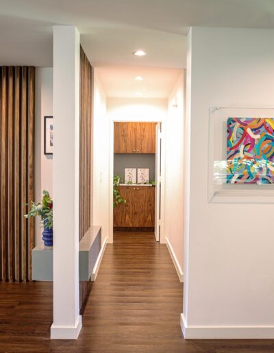 hallway with white walls and wood floors between open living area and dining area, leading to the primary bedroom with built-in wood cabinetry in the entryway