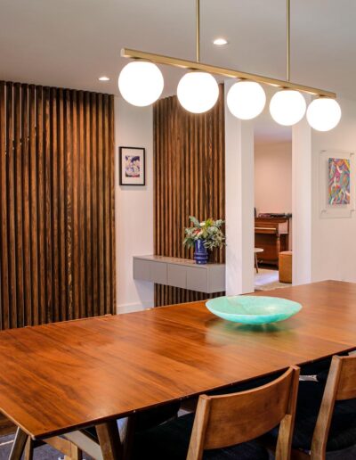 dining room with a Frank Lloyd Write style wall of slotted wood bars and a designer ball glass pendant light fixture above a long wood dining table