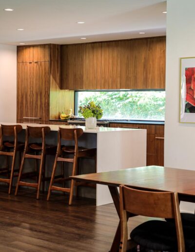 Mid-century modern style kitchen with floor-to-ceiling wood cabinetry, top-of-the-line appliances, a long rectangular window, a wide white stone island, and designer wood barstool chairs