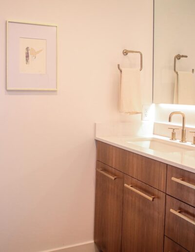 Sleek bathroom vanity with large mirror, under-mirror lighting accents, white stone countertops, wood cabinetry, brushed metal hardware, and an under-mount sink
