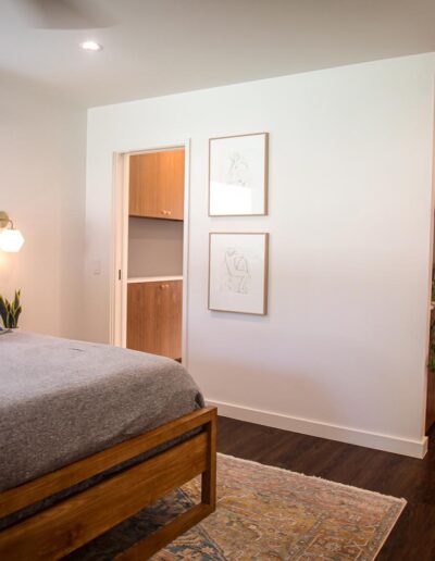 Bedroom with sleek design, white walls, wood floors, and built-in wood cabinetry in the entryway and private bathroom