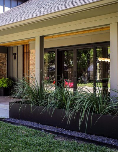 A modern, expansive front porch design with a large box planter, decorative stones, and wide glass doors.